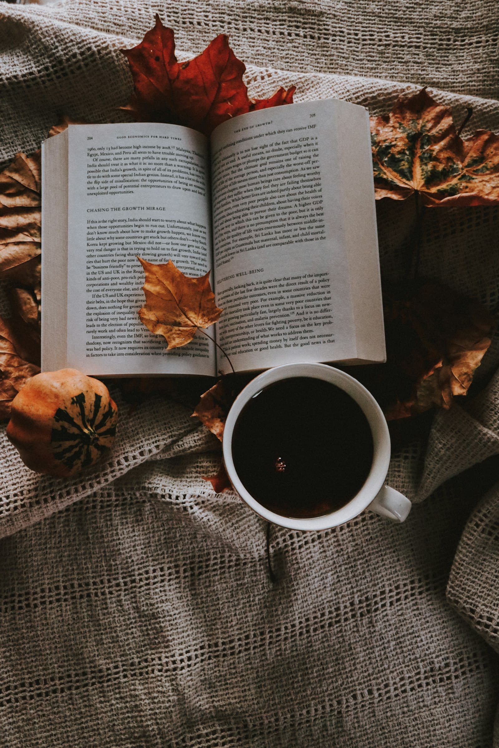 A cup of black coffee on an open book surrounded by autumn leaves